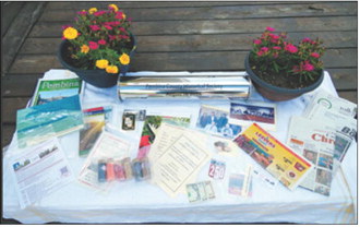 A collection of local memorabilia surrounds a time capsule prepared by the Pembina County Historical Society on Sunday, Aug. 16. The display includes newspapers, photographs, publications, currency and other items representing life in Pembina County in 2026. Photo by Larry Stokke