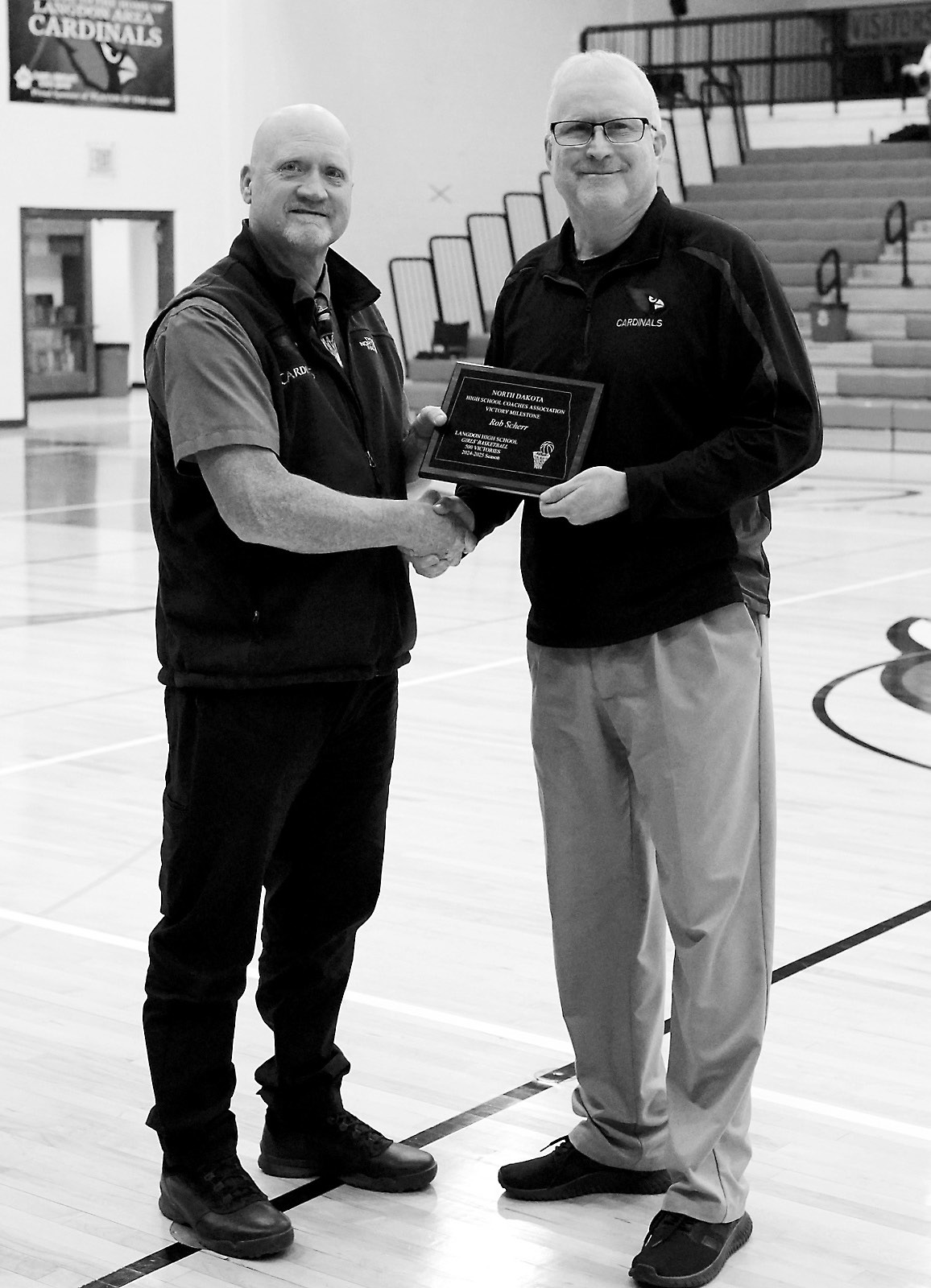 Coach Scherr (right) receives a plaque from Daren Christianson (left) after Scherr reached a milestone with his 500th win during the 2024-2025 Girls Basketball Season. Photo by Larry Stokke.