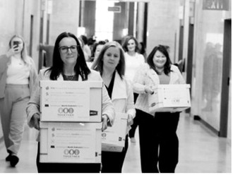 Michelle Wagner, left, carries boxes of signed petitions for a proposed ballot measure to make public school breakfasts and lunches free in North Dakota on April 9, 2026, at the Capitol. To her right is Amy Jacobson and Ashley Gaschk. All three are members of the sponsoring committee for the measure. (Photo by Mary Steurer/North Dakota Monitor)