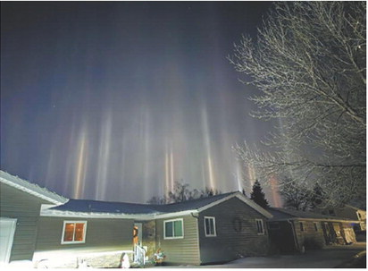 Light pillars rise into the night sky above homes as ice crystals in the cold air reflect nearby lighting sources, creating a rare atmospheric display. Photo by Emily Schaefer