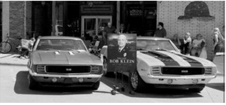 Classic cars line Main Street during the Rendezvous Region Music Fest Rod Run, with a memorial display honoring the late Bob Klein. Photo by Larry Stokke