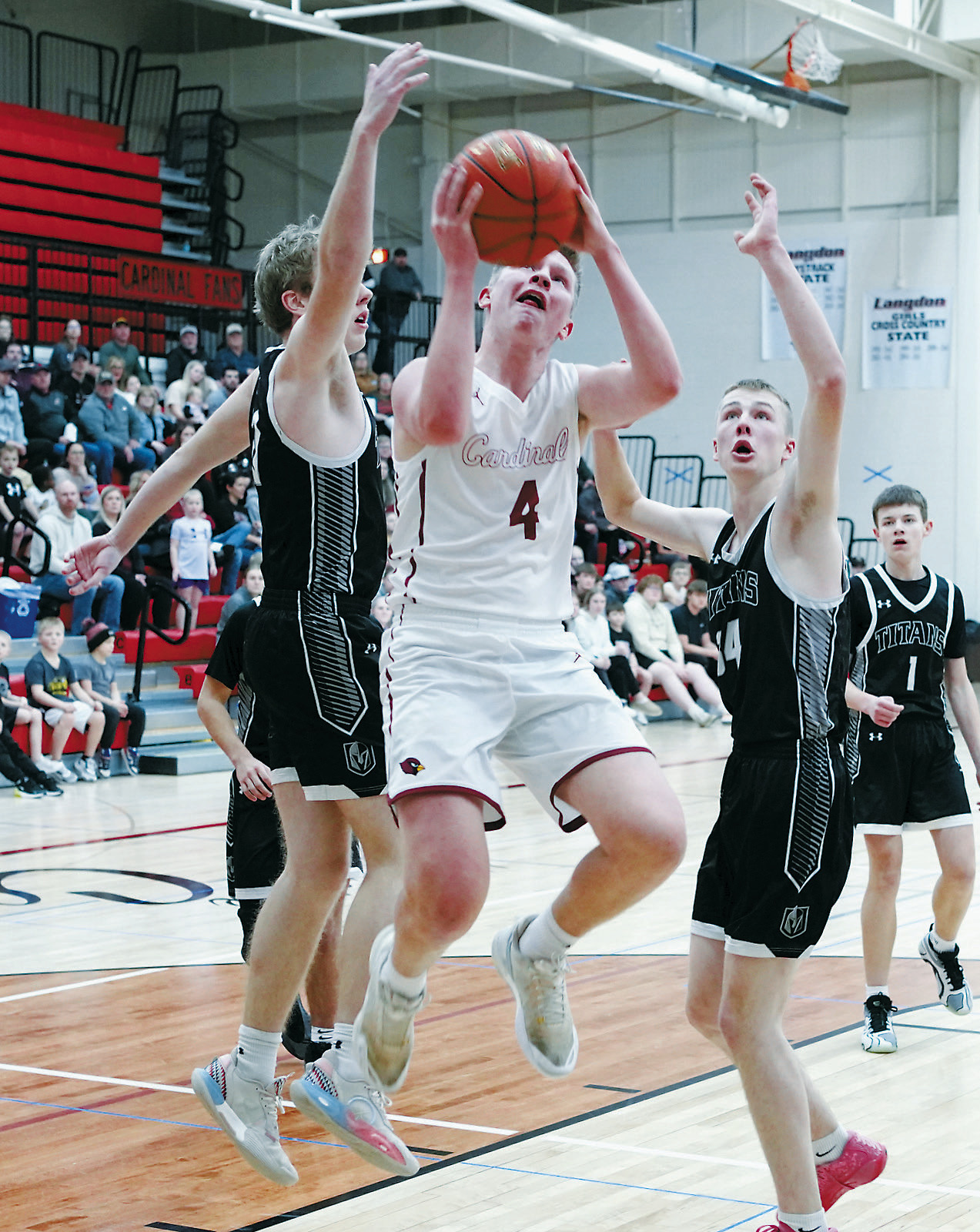 Player of the Game Levi Swanson drives to the net and splits two Titan defenders, dropping in a basket in the Cards win at Langdon over the DVE Titans. Photo by Larry Stokke.