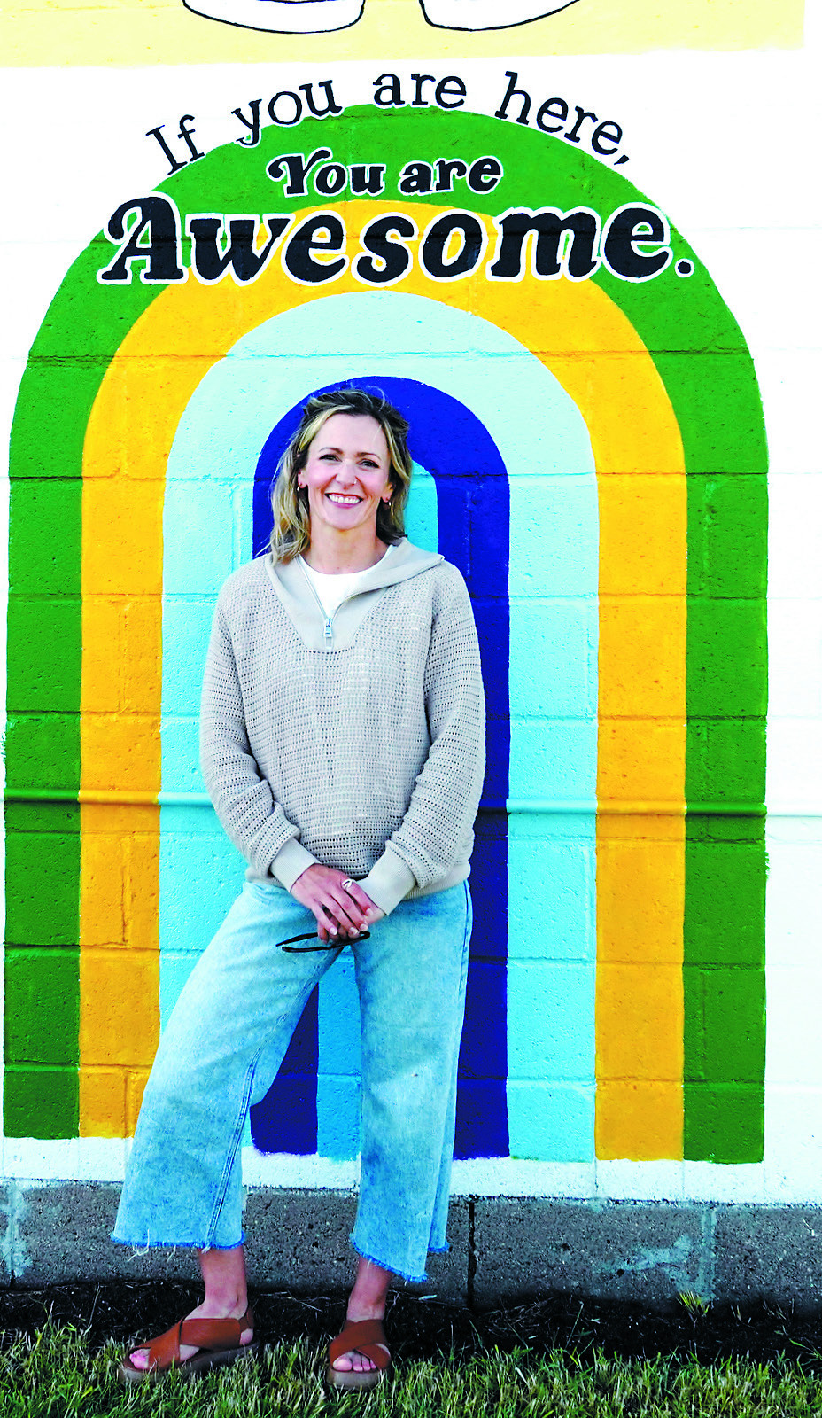 Mural artist Kassie Zimmer Lee poses in front of a portion of the new Munich mural she designed and painted. A Munich native, Lee incorporated community ideas and local themes into the artwork, which was unveiled June 24 in downtown Munich. Photo by Larry Stokke community for the support of the artistic while offering residents and visitors a vibrant new destination for years to come.