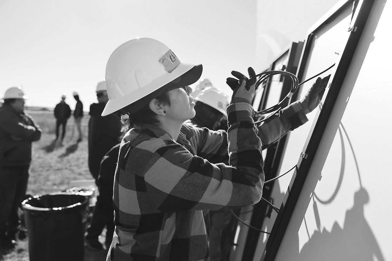 A technician trainee with nonprofit Indigenized Energy inspects wiring for a ground-mounted residential solar project installed at the Pine Ridge Reservation, home of the Oglala Sioux tribe, in October 2024. Residents using the solar system will be able save around $1,200 per year in utility costs, according to estimates from the nonprofit. Photo provided.