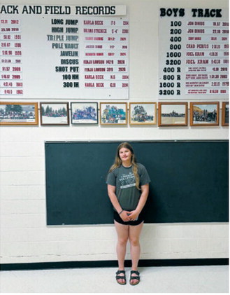 Fenja Lawson stands beneath the Langdon Area/Munich school track and field record board, where she now holds the school records in both the discus (142 feet, 9 inches) and shot put (39 feet, 9 inches). Lawson recently qualified for the AAU National Junior Olympic Games and the USATF National Junior Olympic Track &amp; Field Championships. Submitted photo