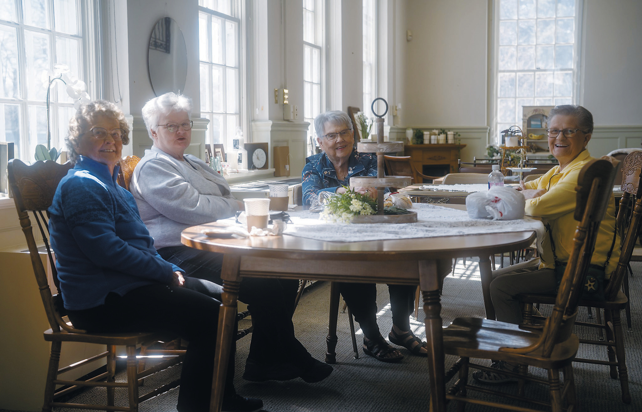 A group of ladies, including Gladys Kemnitz, who was Coffee, Thrift, and Gift’s first customer (left, in blue), enjoy a cup of coffee in the shop’s gathering area. Photo by Jesus Ramos.