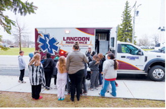 Students gather around an ambulance during Elementary School Safety Day as EMS personnel explain emergency equipment, ambulance operations and the role of first responders in the community. Photo by Larry Stokke