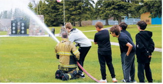 A local volunteer firefighter demonstrates firefighting techniques as students participate in a hands-on fire safety activity during Elementary School Safety Day. Photo by Larry Stokke