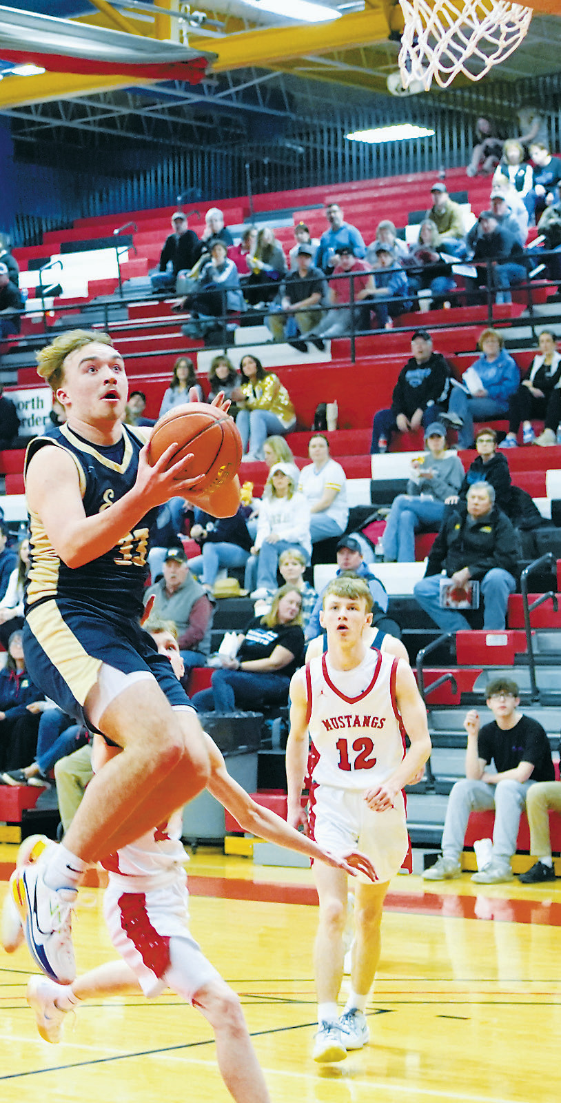 Kade Schafer flies into the lane and drops in a basket, finishing the game with 13 points versus Midway Minto. Photo by Larry Stokke.