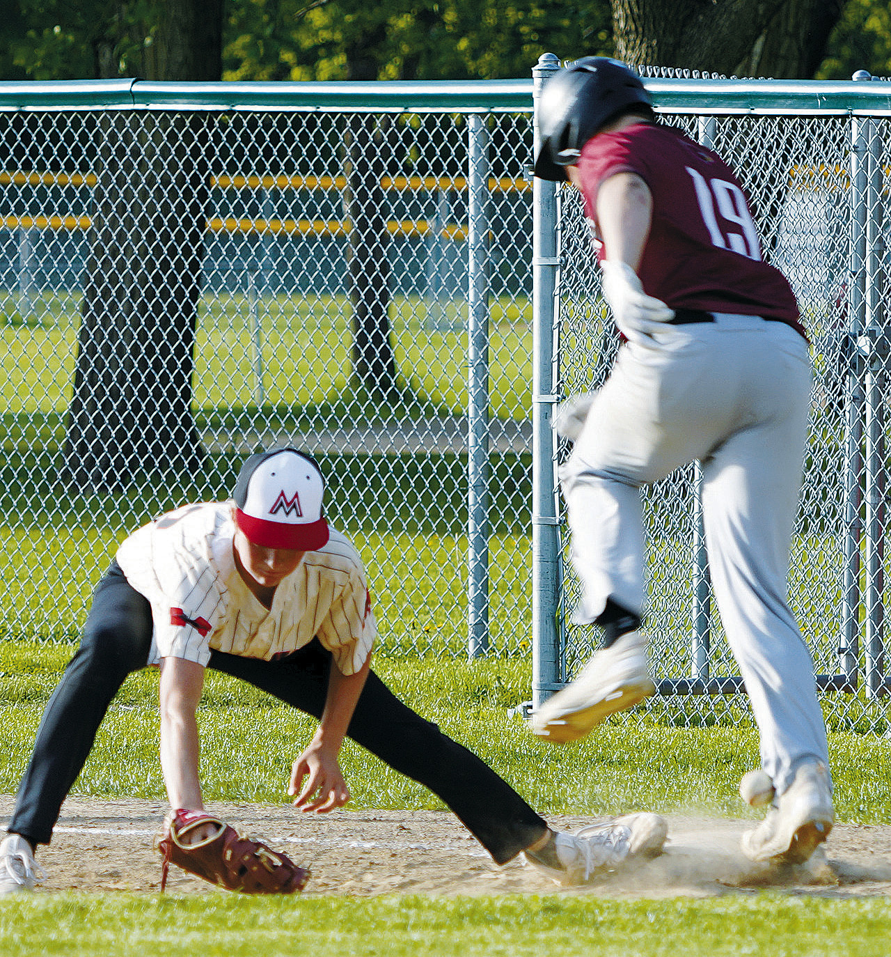 Landon Schneider gets nailed in the right ankle as he gets on 1st base against Midway-Minto. Photo by Larry Stokke.