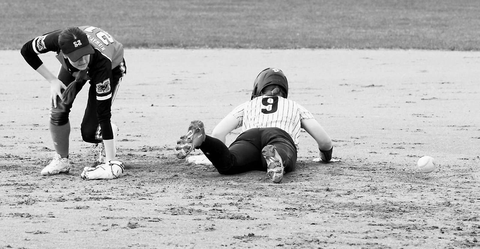 Hannah Moore gets safely back to base on a bad throw against Midway-Minto in Minto. Photo by Larry Stokke.