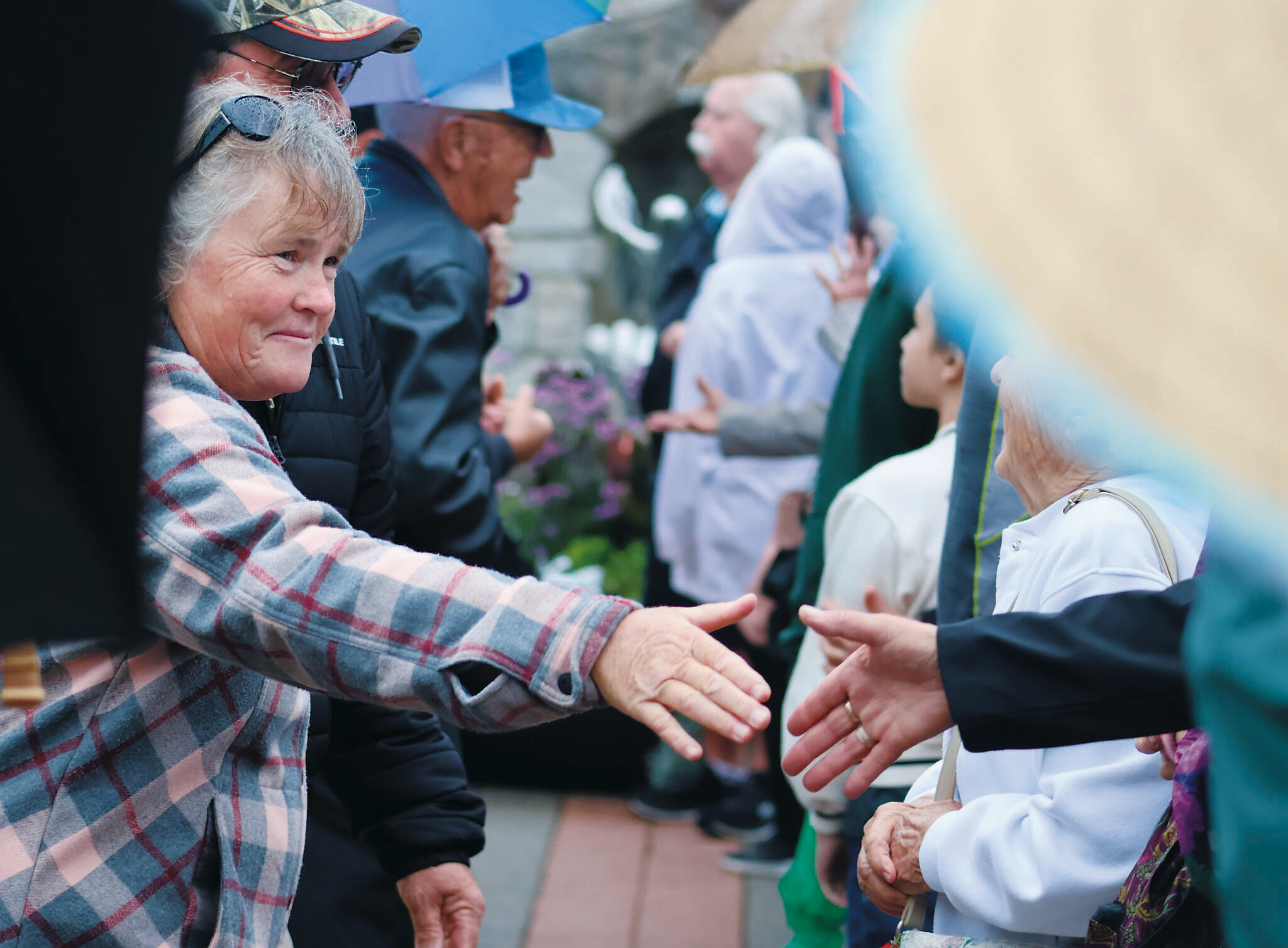 Canadians and Americans reach across the border to shake hands in an event celebrating friendship between the two nations at the International Peace Garden on Aug. 9, 2025. (Photo by Mary Steurer/North Dakota Monitor)