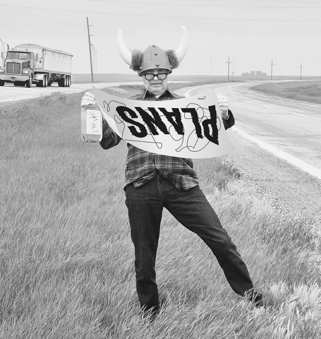 An unidentified alleged highway engineer at Nekoma Confusion Corner holding plans and a fine bottle of Bourbon.