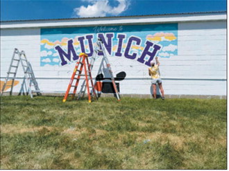 The first letters of “Munich” begin to appear as artist Kassie Zimmer Lee works on the community mural north of the Munich Plaza. The project is being coordinated with the Rendezvous Region Tourism Council. Submitted photo