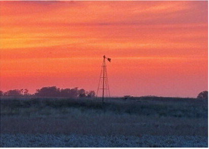 An old farm windmill stands silhouetted against a colorful prairie sunset, a reminder of the agricultural heritage that continues to shape the Borderland landscape. Submitted photo
