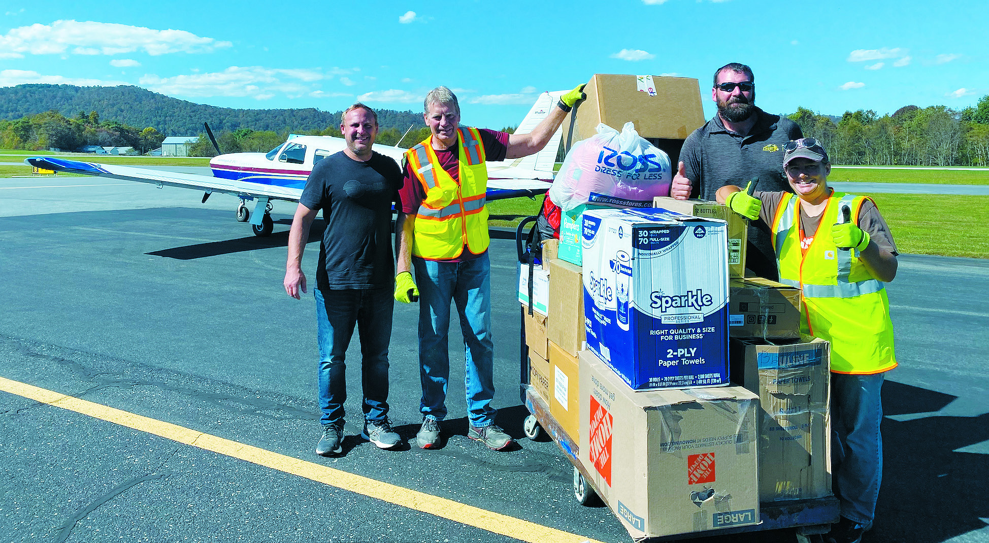 Casey Veil (left, black shirt) and Treven Iverson (right, sunglasses) of Jamestown pose with volunteers and the supplies they flew into a distribution point in Jefferson, N.C. on Oct. 5. Contributed by Veil.