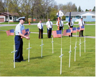 Brock Freer of the U.S. The Coast Guard places flags at crosses honoring area residents who have died during the past year as part of Langdon's Memorial Day observance. Freer, home on military leave, assisted with the annual tribute alongside members of the American Legion honor guard. Photo by Larry Stokke