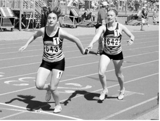 Emersen Helgoe hands the baton to Shirley Kemp during the 4x400-meter relay. The Pembina County North quartet of Maci Puppe, Delaney Denault, Emersen Helgoe and Shirley Kemp finished in 4:19.70 at the NDHSAA Class B State Track and Field Meet. Photo by Larry Stokke