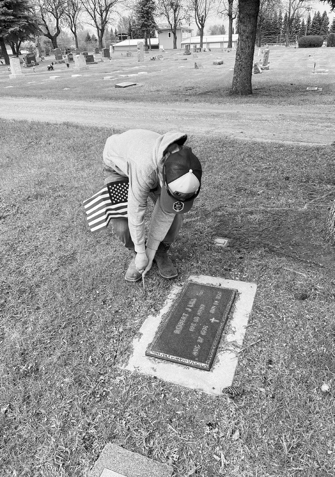 4-H member Carl Henry places a flag at a gravesite for Memorial Day.