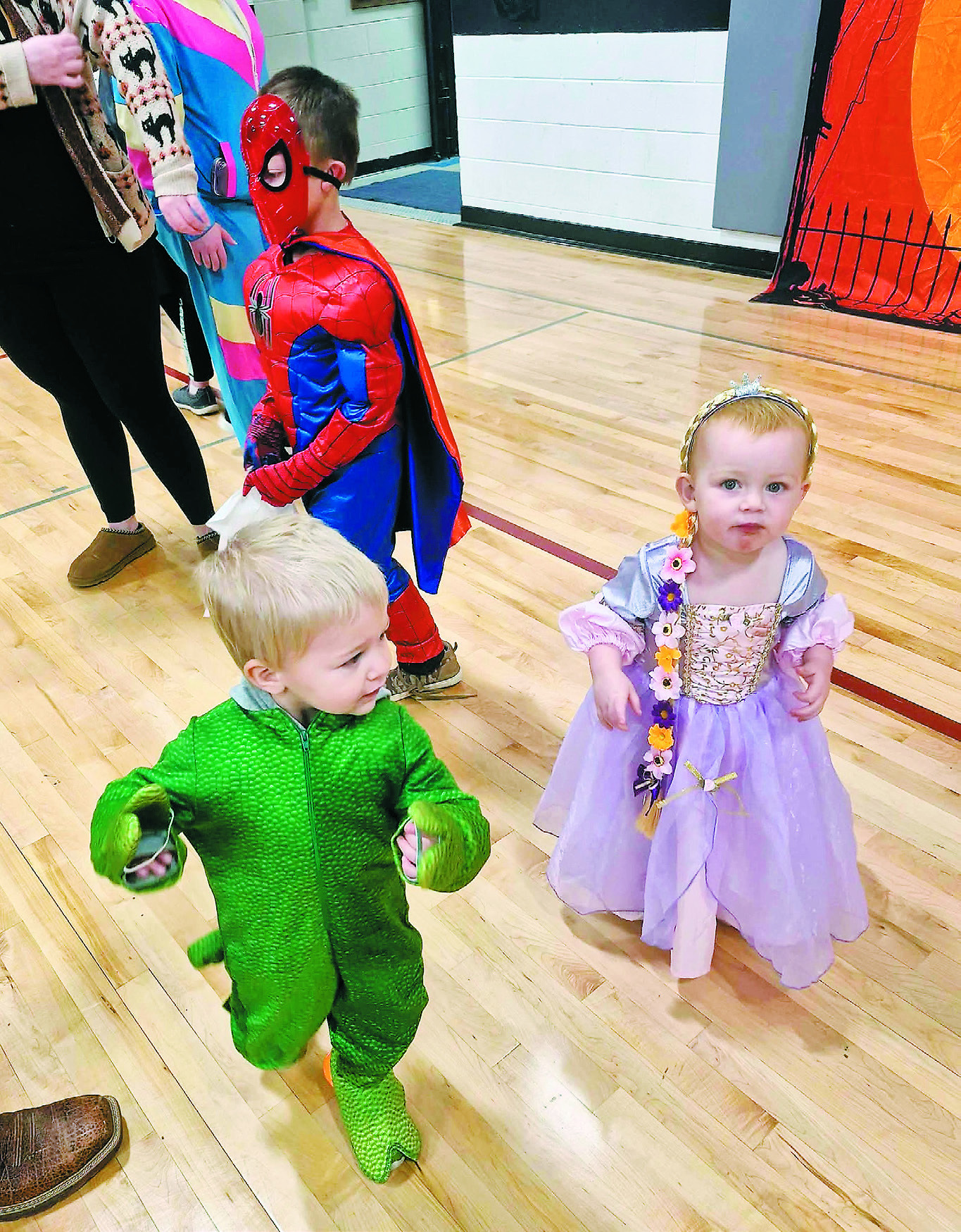Winston dressed as Spiderman, Oliver dressed up as a dinosaur, and little Kyrbie as a princess, all dance together, likely celebrating their full bags of candy!