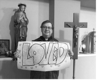 Father Phil Ackerman holds a handmade 'Loved' sign given to him by parishioners from St. Alphonsus Parish in Langdon. The keepsake is one of many reminders of the friendships he formed during his years serving the community. Submitted photo