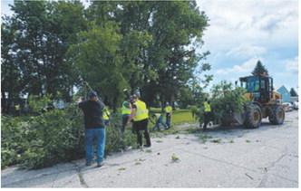 Volunteers and heavy equipment operators work to clear storm debris from a Milton street following severe weather that damaged trees throughout the community on June 10. More than 40 volunteers participated in the cleanup effort.