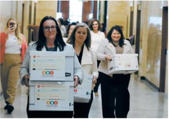 Michelle Wagner, left, carries boxes of signed petitions for a proposed ballot measure to make public school breakfasts and lunches free in North Dakota on April 9, 2026, at the Capitol. To her right are Amy Jacobson and Ashley Gaschk, other members of the measure's sponsoring committee. Together for School Meals has reported nearly $1.1 million in monetary support for the measure. (Photo by Mary Steurer/North Dakota Monitor)