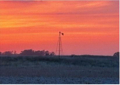 An old farm windmill stands silhouetted against a colorful prairie sunset, a reminder of the agricultural heritage that continues to shape the Borderland landscape. Submitted photo