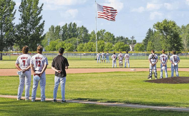 Players stand facing the flag as the National Anthem plays at the start of the game against Midway/Minto on June 30 in Langdon. PHOTO BY LARRY STOKKE.