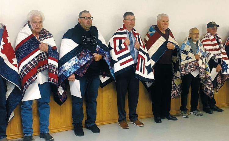 Fall of 2025 Quilts of Valor recipients (L-R) Jim Swenson (Army), Earl Steinke (Army), Scott Anderson (Army), Daniel Haugen (Marine), Bennett Spenst (Army), Bob Tapson (Army), Roger Kram (Navy), and Benjamin Bim Perius (Army). Photo by Gael Balsdon.