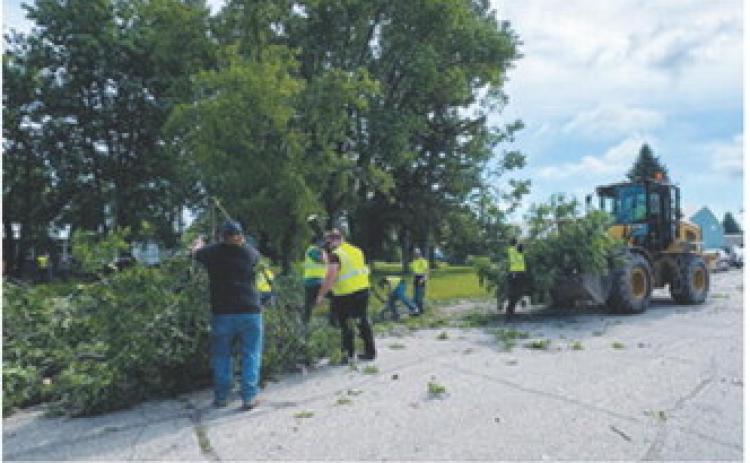 Volunteers and heavy equipment operators work to clear storm debris from a Milton street following severe weather that damaged trees throughout the community on June 10. More than 40 volunteers participated in the cleanup effort.