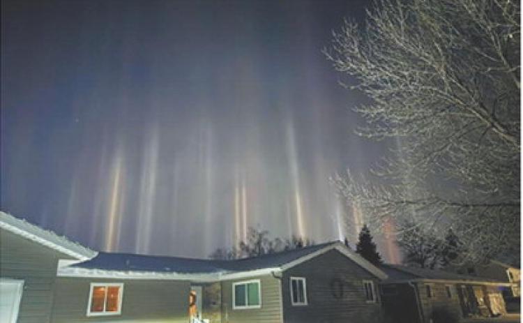 Light pillars rise into the night sky above homes as ice crystals in the cold air reflect nearby lighting sources, creating a rare atmospheric display. Photo by Emily Schaefer