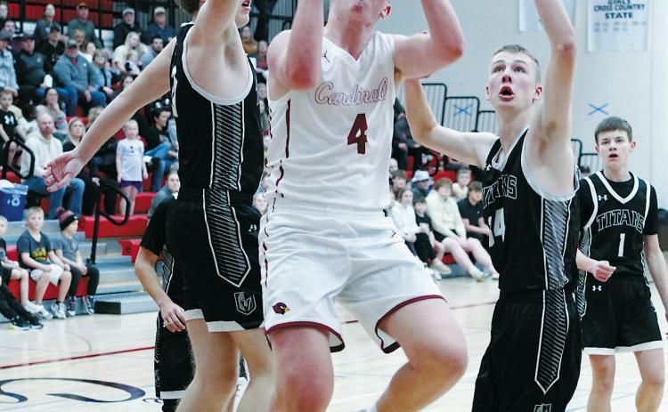 Player of the Game Levi Swanson drives to the net and splits two Titan defenders, dropping in a basket in the Cards win at Langdon over the DVE Titans. Photo by Larry Stokke.
