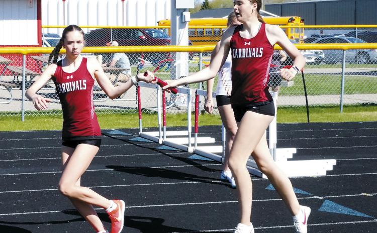 Taya Feist hands the baton to Olivia Lorenz who, along with Hallie Overby and Mya Swanson, placed first in the 4X800 relay on April 5. Photo by Larry Stokke.
