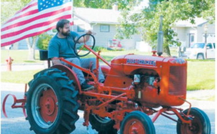 A vintage Allis-Chalmers tractor carrying an American flag makes its way through the Pre-Blast Bash parade. Photo by Larry Stokke