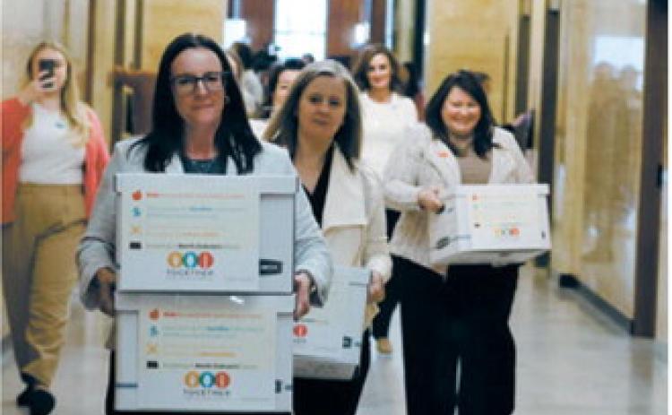 Michelle Wagner, left, carries boxes of signed petitions for a proposed ballot measure to make public school breakfasts and lunches free in North Dakota on April 9, 2026, at the Capitol. To her right are Amy Jacobson and Ashley Gaschk, other members of the measure's sponsoring committee. Together for School Meals has reported nearly $1.1 million in monetary support for the measure. (Photo by Mary Steurer/North Dakota Monitor)