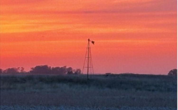 An old farm windmill stands silhouetted against a colorful prairie sunset, a reminder of the agricultural heritage that continues to shape the Borderland landscape. Submitted photo