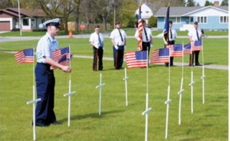 Brock Freer of the U.S. The Coast Guard places flags at crosses honoring area residents who have died during the past year as part of Langdon's Memorial Day observance. Freer, home on military leave, assisted with the annual tribute alongside members of the American Legion honor guard. Photo by Larry Stokke
